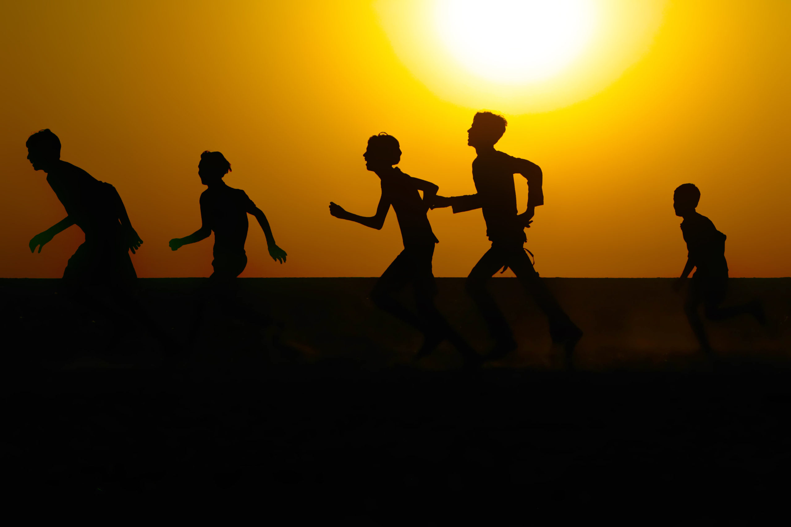 Silhouettes of young athletes running outdoors.